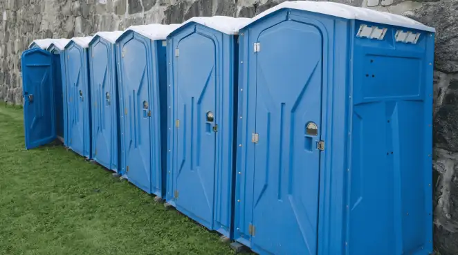 Row of blue portable toilets lined up on grass against a stone wall for event sanitation in New Haven, CT