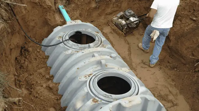 Septic tank installation showing a technician compacting soil around a new poly septic tank in an excavation pit in New Haven, CT